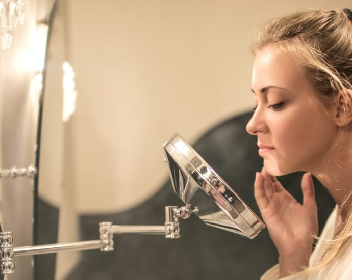 Image shows a woman examining her acne in a bathroom mirror